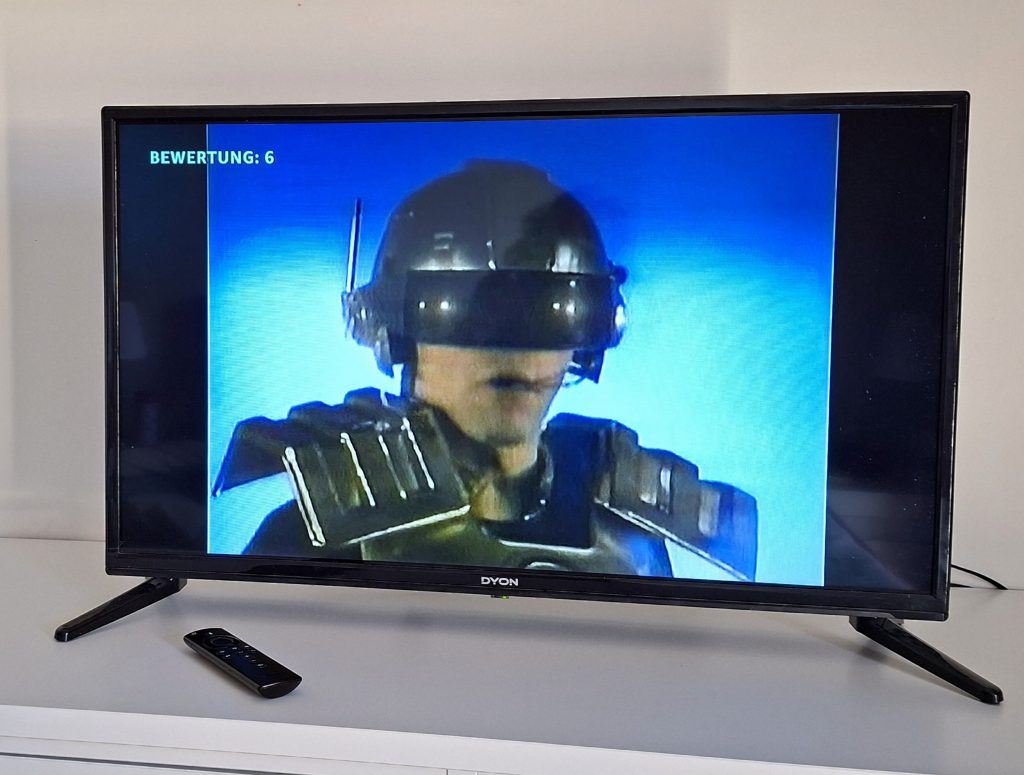 Szene aus der Science-Fiction-Serie Captain Power auf einem Fernseher mit futuristisch gekleideter Figur und blauem Hintergrund.