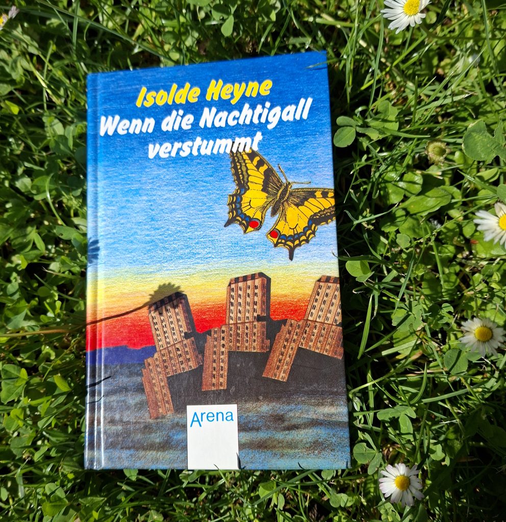 Buch „Wenn die Nachtigall verstummt“ von Isolde Heyne auf einer Wiese mit Gänseblümchen und Klee liegend.